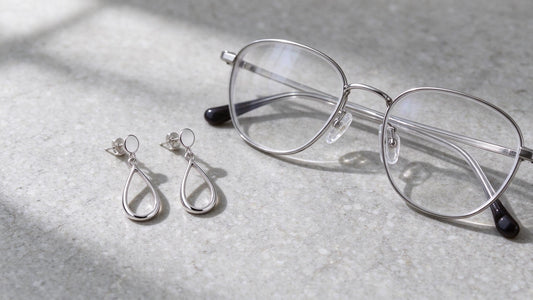 Elegant sterling silver earrings displayed beside stylish glasses frames on a neutral background