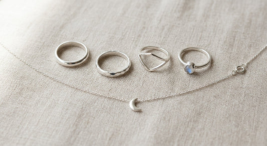 Polished sterling silver rings and delicate chain necklace on neutral linen.