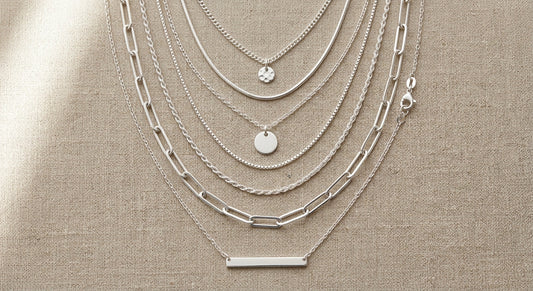 Curated sterling silver necklaces layered on a neutral linen background