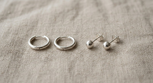 Minimalist sterling silver stud and hoop earrings on neutral linen