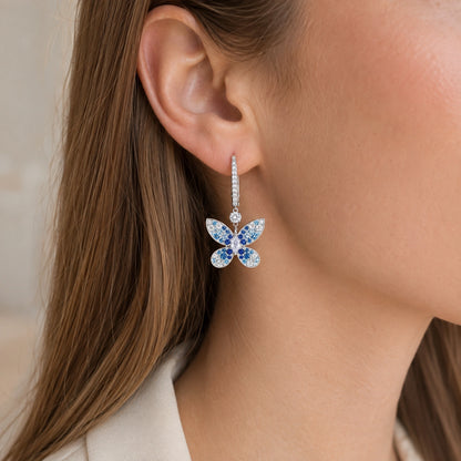 Close wearing view of a blue butterfly drop earring on an adult Western model