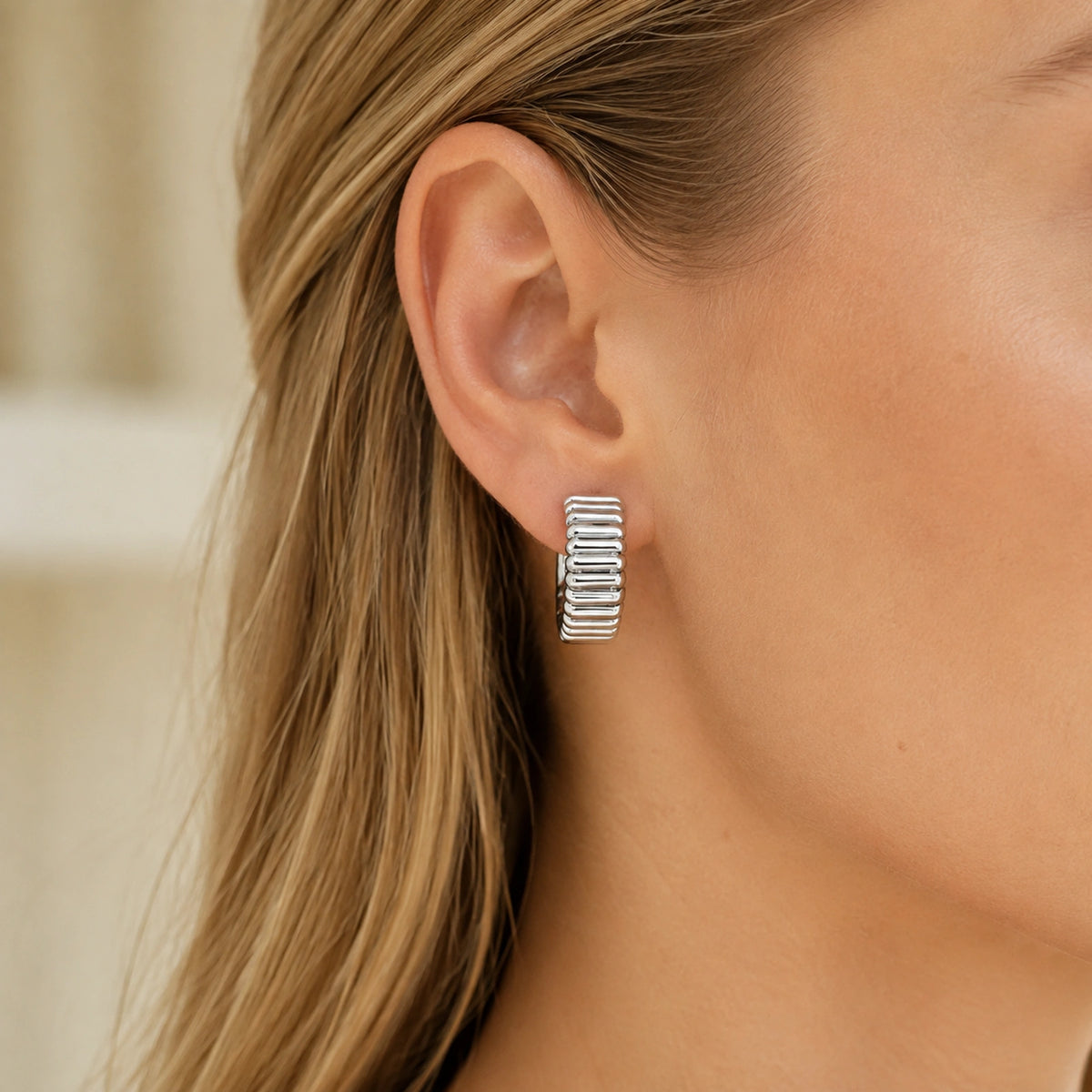 Ribbed silver wide half-hoop earring worn close up by a Western woman