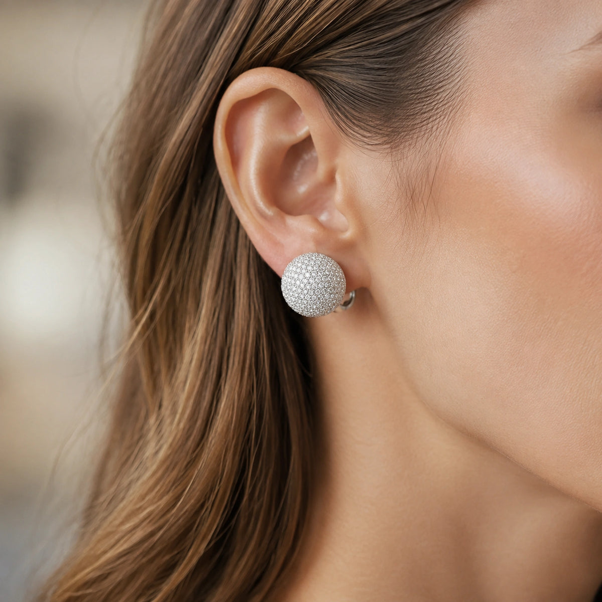 Close wearing view of a round pave dome huggie earring on an adult Western model