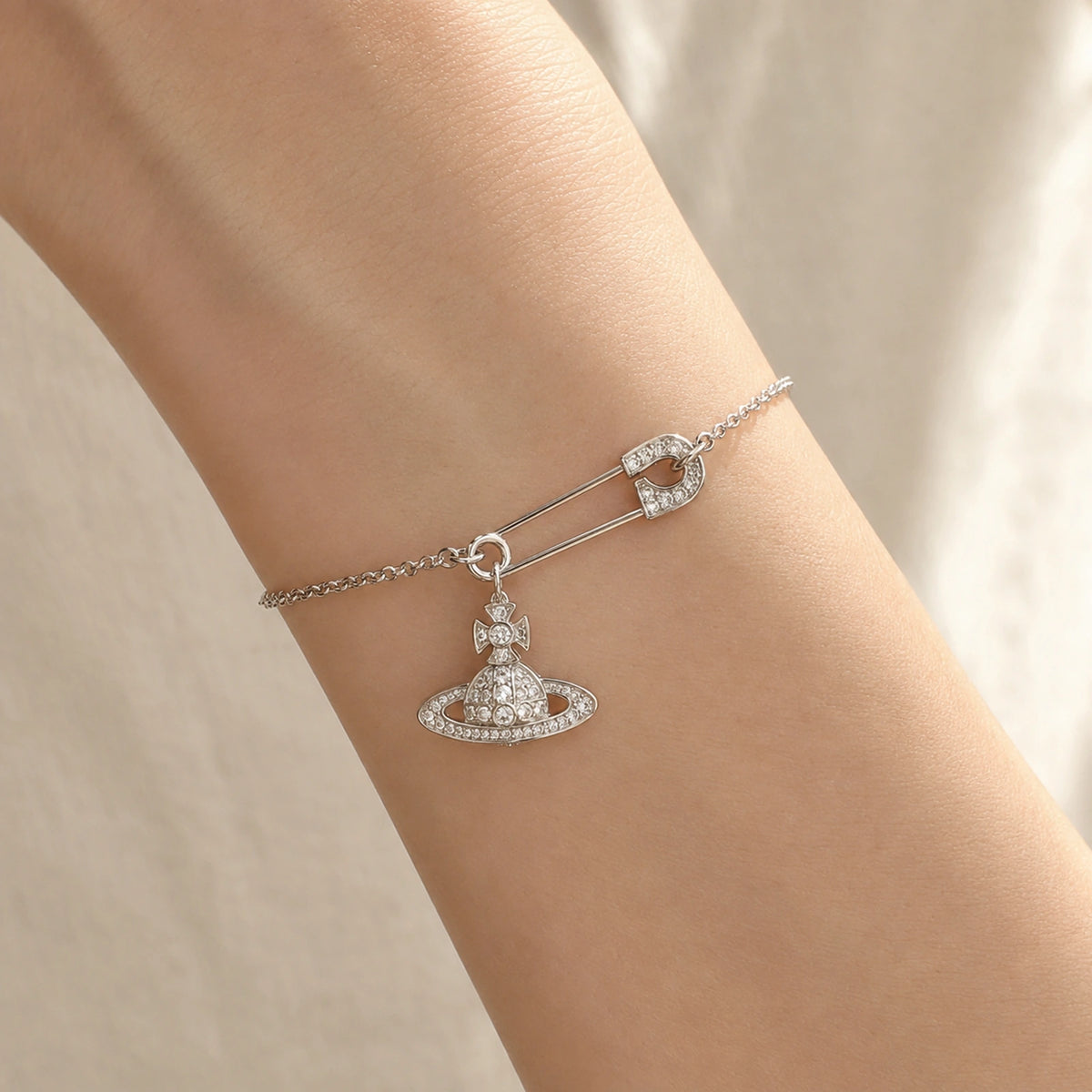Close wrist view of a delicate silver-tone safety pin orb charm bracelet.