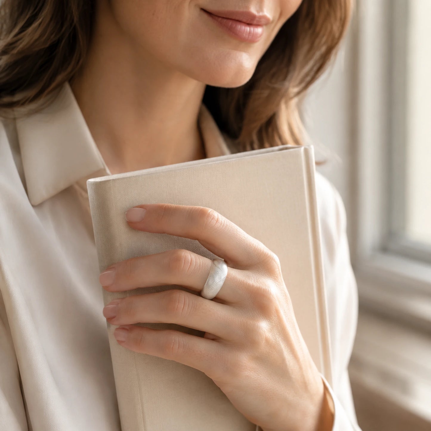 Woman wearing a wide silver fingerprint texture ring by a window