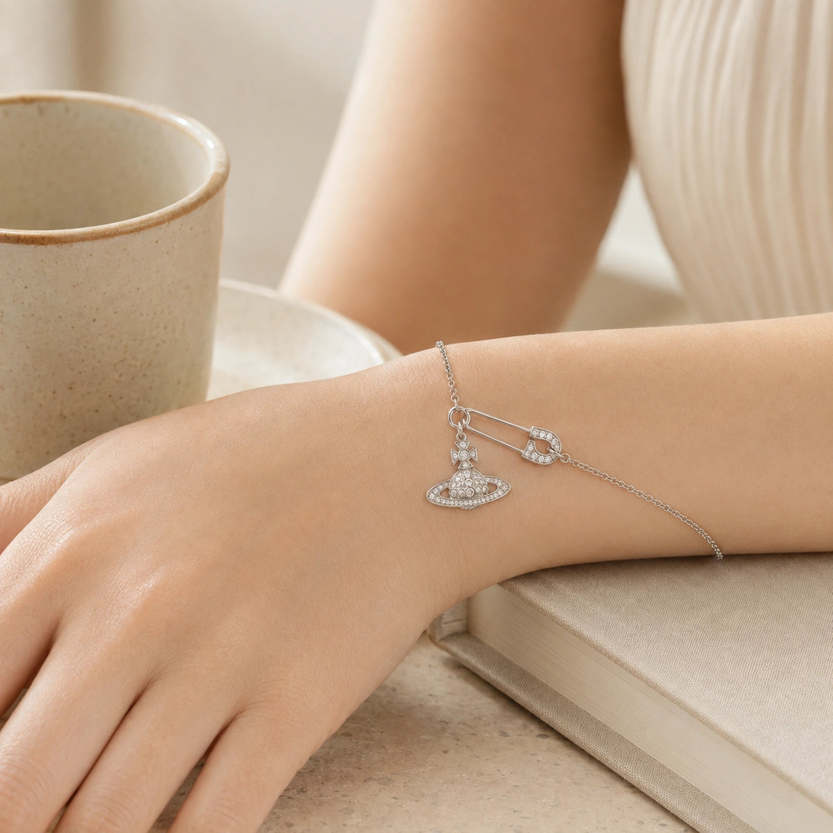 Woman wearing a silver-tone safety pin orb charm bracelet in a warm lifestyle setting.