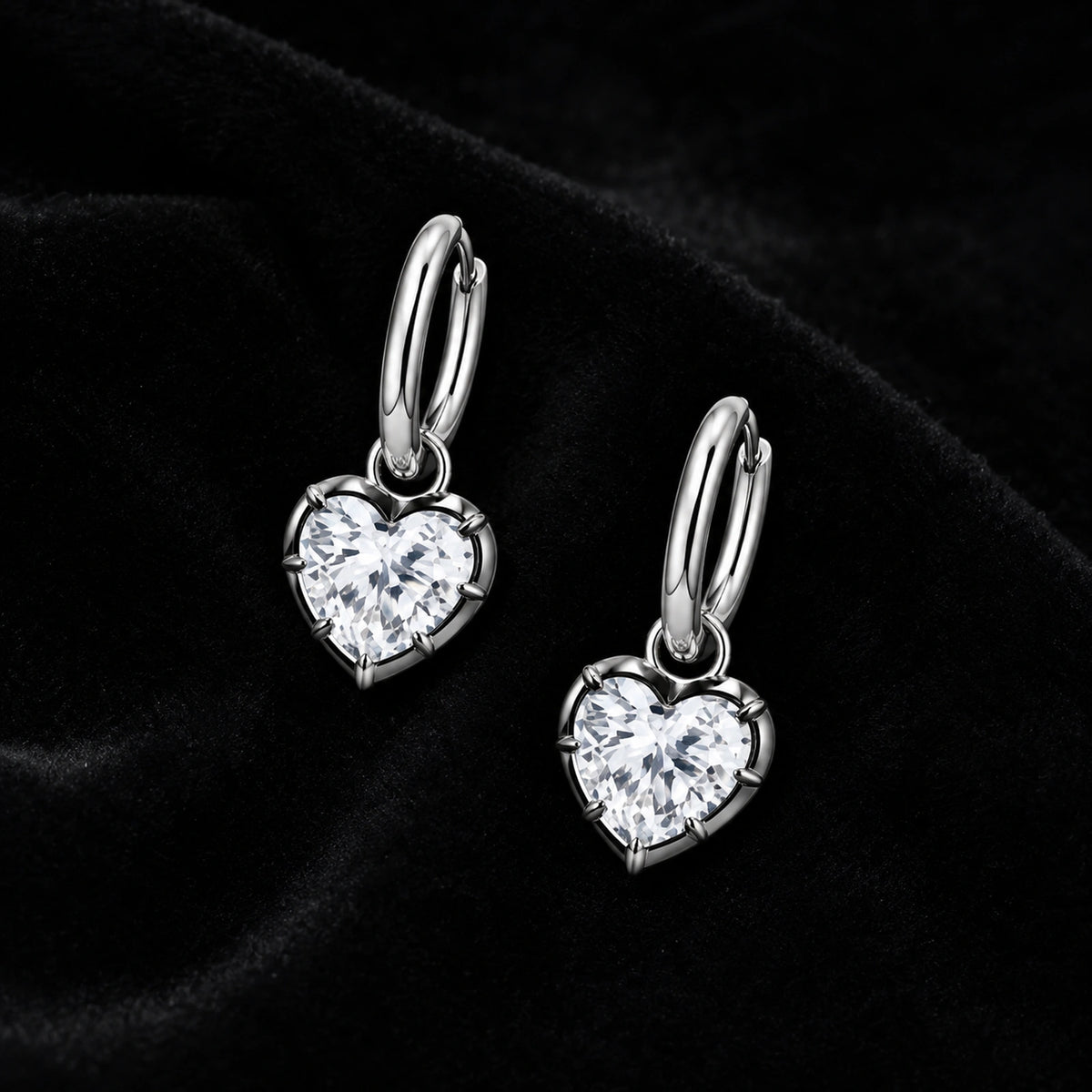 Pair of silver heart crystal huggie earrings on black velvet