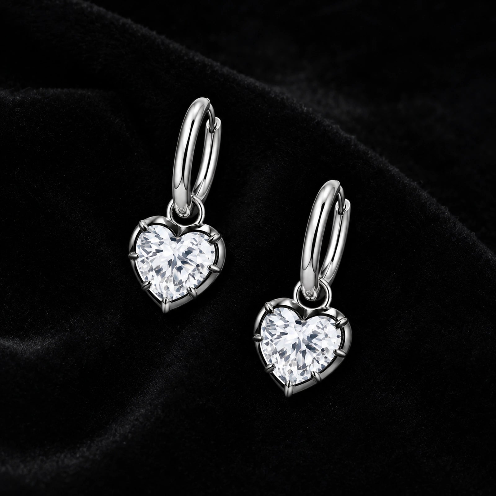 Pair of silver heart crystal huggie earrings on black velvet