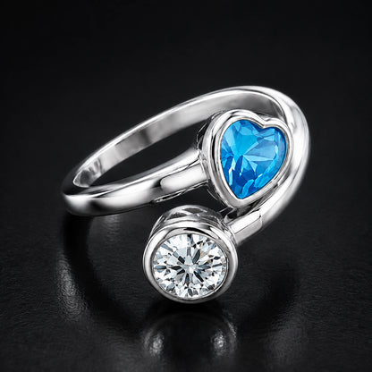 Blue heart and clear round accent silver bypass ring on a dark background